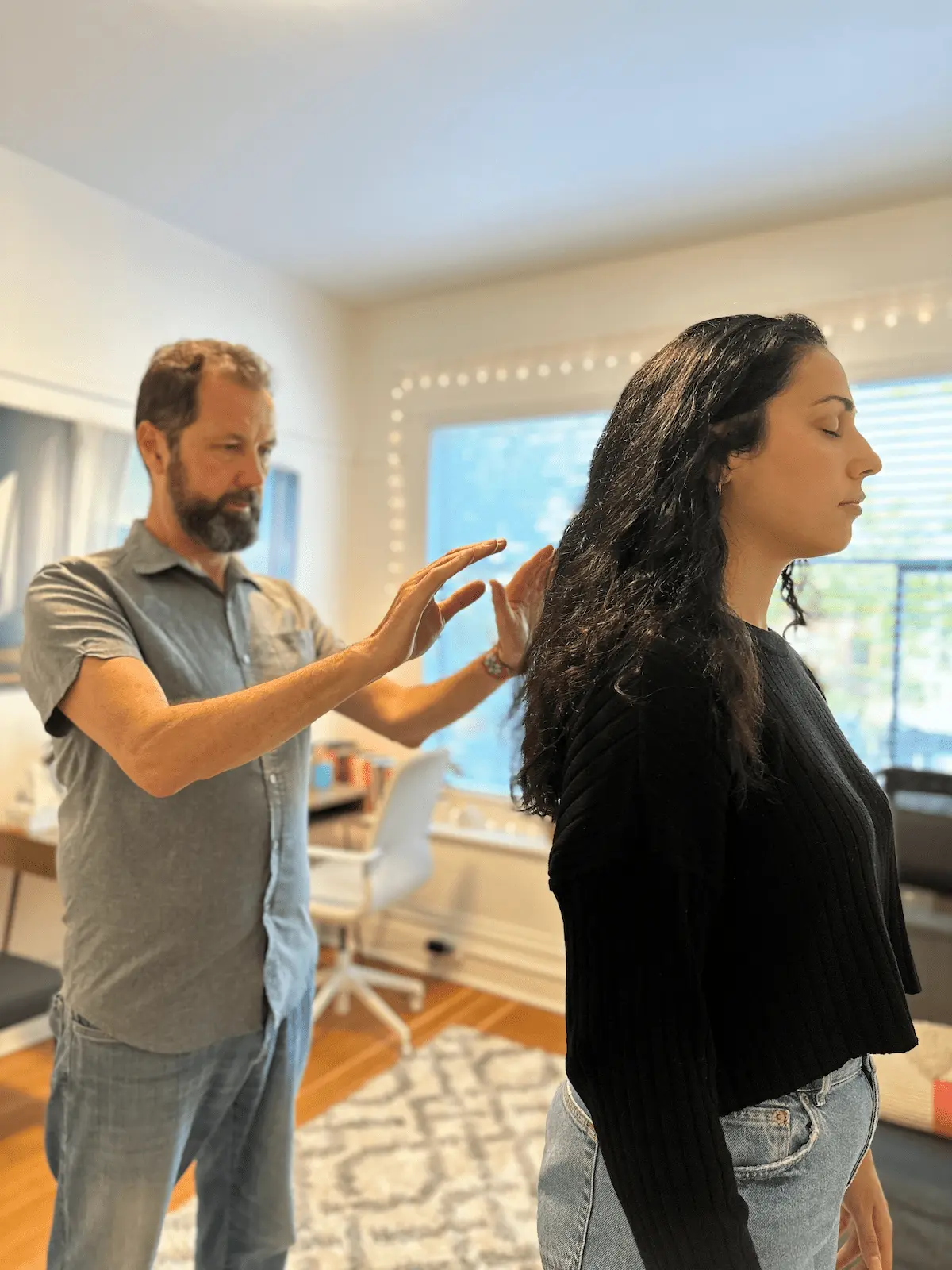 A man holds his hands behind a woman's shoulders as she stands with her eyes closed.